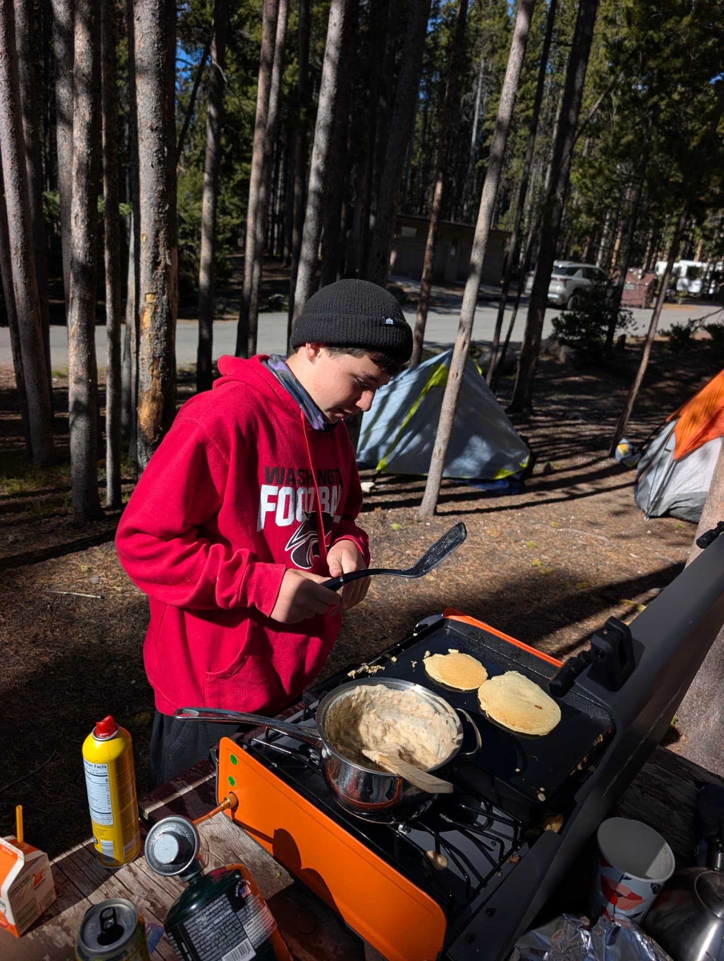 A teenager cooking pancakes on a camp griddle in the woods