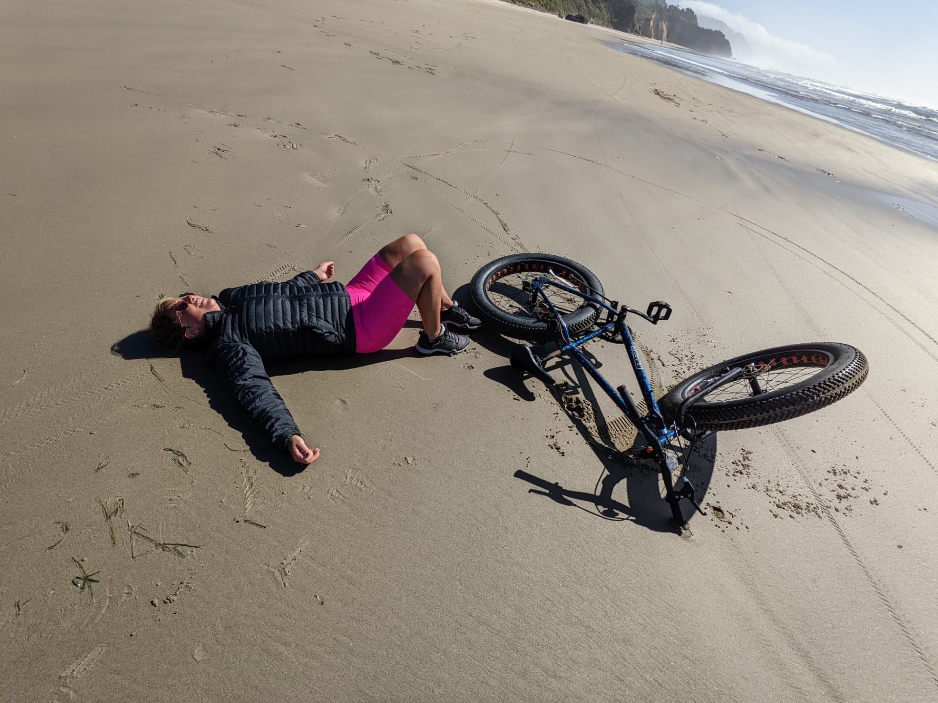 Leah lying on a sandy beach next to her bike, arms spread out